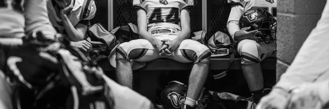 Intense black and white photo captures high school football players in a locker room pre-game.