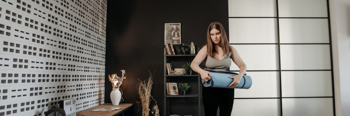 Plus size woman rolling a yoga mat in a stylish indoor setting with modern decor.